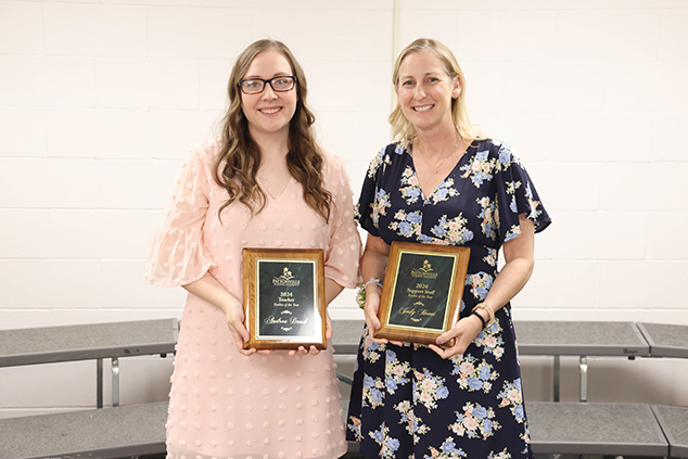 Two staff members stand with plaques after winning an award