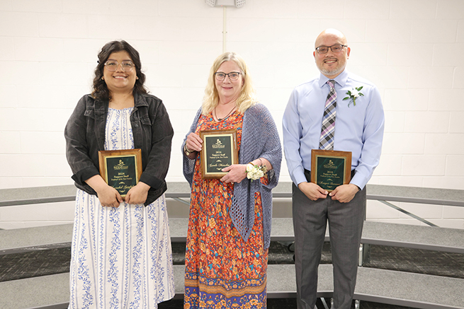 Three staff members stand with plaque